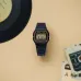 Flat lay of Casio F-91WG-9QDF Watch with gold accents on beige surface surrounded by vinyl record and cassette tapes.