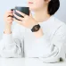 Wrist view of Casio F-91WG-9QDF Watch with black strap and gold accents while holding a gray mug in casual setting.