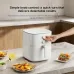Front angled view of Xiaomi Air Fryer Essential 6L with hand adjusting knob beside skewers, wings, and fries.