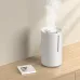 Xiaomi Smart Humidifier 2 placed on wooden surface emitting mist beside a book titled A Smile in the Mind.