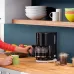 Lifestyle view of Braun Breakfast1 KF1100 Coffee Maker with person pouring coffee into green mug in kitchen.