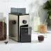 Lifestyle view of DeLonghi KG89 Coffee Grinder on kitchen counter with beans, sugar, milk, and fresh coffee nearby.