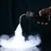 Angled view of the Ulanzi FM01 Fog Machine in use, emitting dense vapor through a bent nozzle onto a surface below.