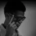 A black and white photo of a man wearing Zeblaze AI Shooting Glasses, touching the side to activate a function.
