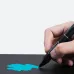 Huion Inspiroy Dial 2 Graphics Tablet stylus shown drawing on the tablet surface in close-up view.