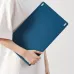 Person holding a slim blue drawing tablet against a white outfit, showing the back design with clean, minimal look