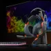 Desk setup view of the Meetion MT‑HP099 RGB 7.1 Surround Sound USB Gaming Headset on stand beside monitor with colorful visuals.