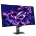 An angled front view of the black ASUS ROG Strix OLED XG32UCDS monitor on its stand, displaying a purple/pink ROG logo and glowing particles on the screen.