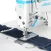 Close-up of the white Jack A4C-C sewing machine head stitching two pieces of dark blue denim fabric on a white tabletop.
