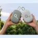 Two Soundcore Select 4 Go speakers, one gray and one white, are held up against a blurred natural background.