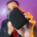 Close-up of a hand holding the QCY SP2 Portable Bluetooth Speaker showing its textured black design against a colorful background.