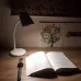 White desk lamp illuminating a workspace with pencils, a notebook, and a wooden desk.