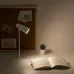 Workspace view of Xiaomi Flexible Rechargeable Lamp lighting open book on desk with plant and corkboard background.