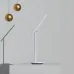 Minimalist view of Yeelight Z1 Pro Table Lamp angled on gray surface with golden hanging spheres in background.