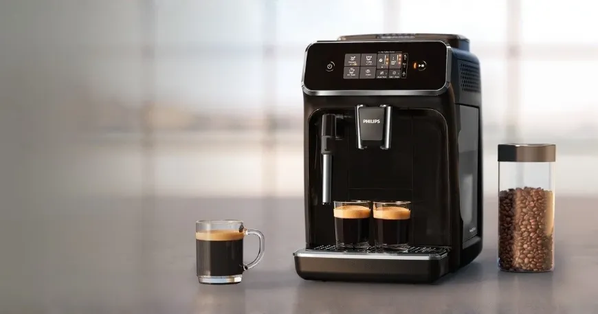 Angled view of a black Philips EP2220/10 automatic coffee machine on a kitchen counter next to coffee cups and beans.